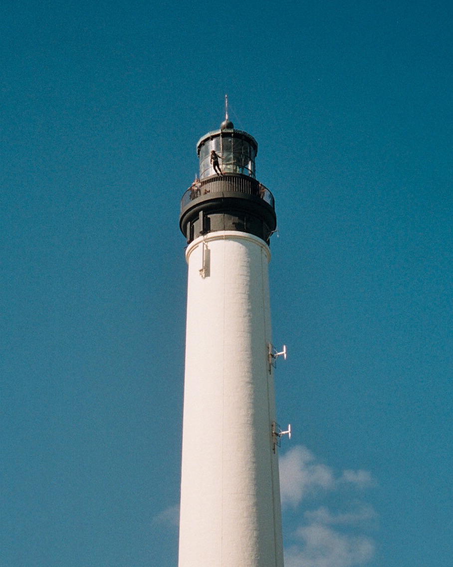 A jumper on the railing of a white lighthouse under a blue sky