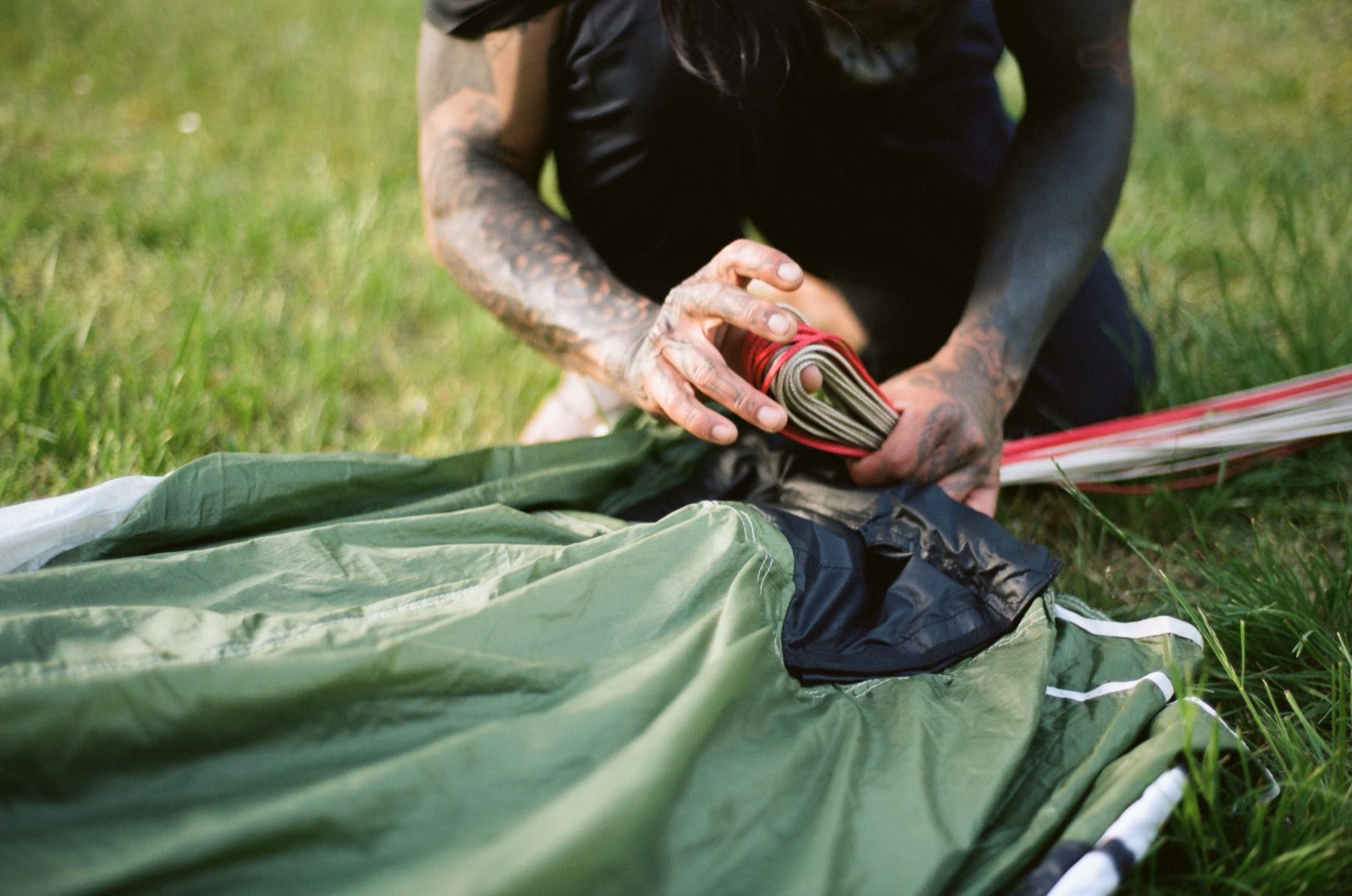Dee's tattooed hands packing a parachute on the grass