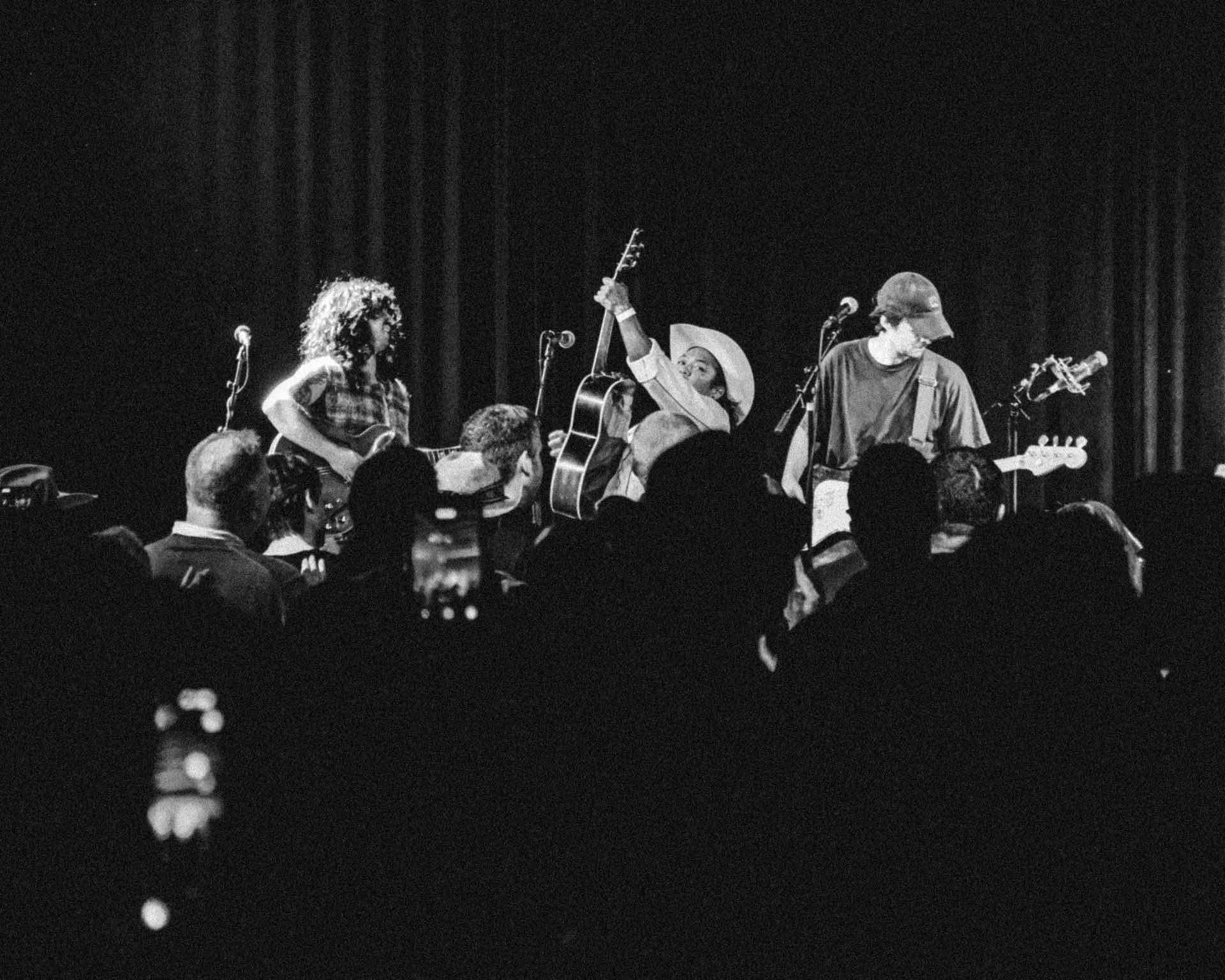 Johnny Devils on stage in front of a crowd, the guitarist in a cowboy hat raising his guitar, black and white