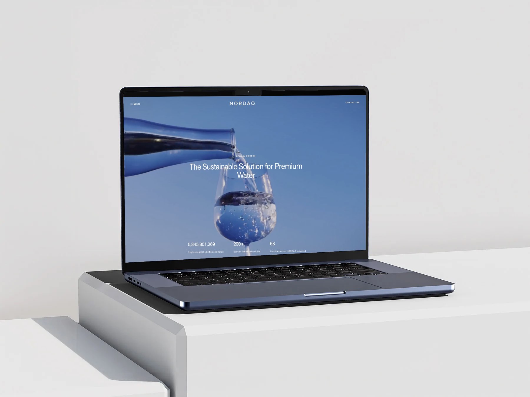 The Nordaq home page on a MacBook on a white plinth, water poured into a glass under Sustainable Solution for Premium Water