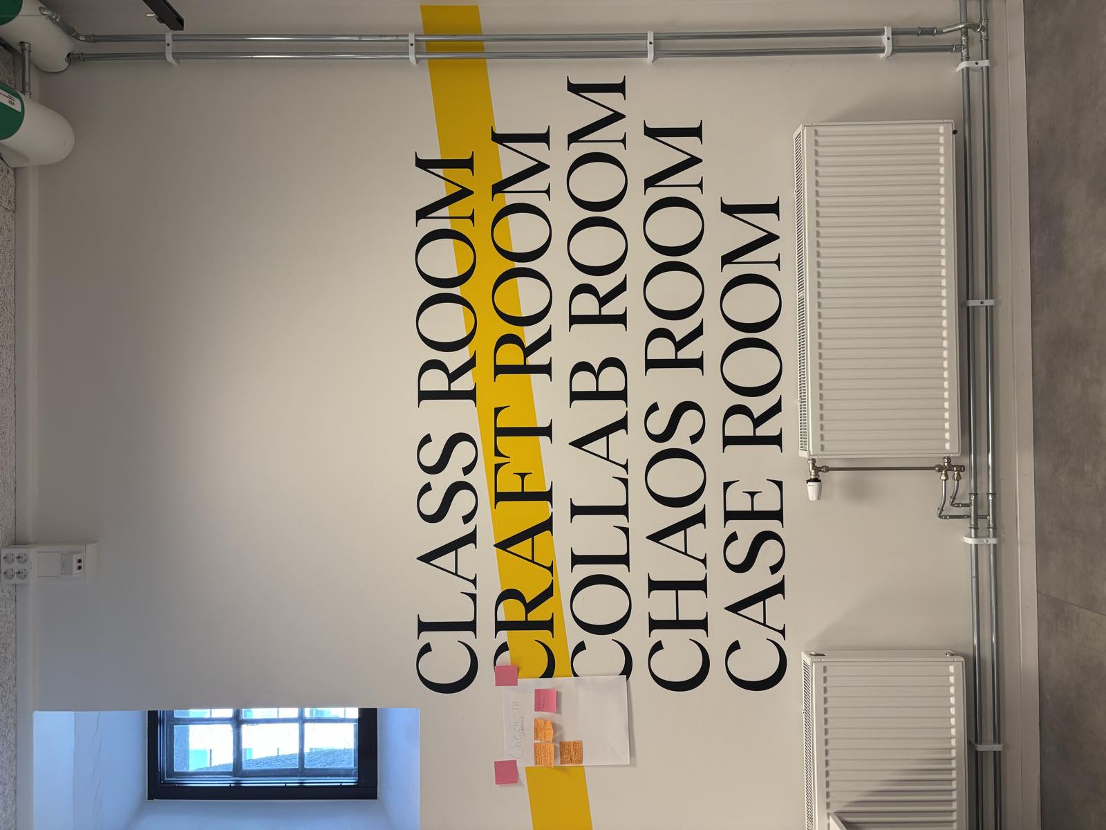 A wall at Berghs that reads class room, craft room, collab room, chaos room, case room