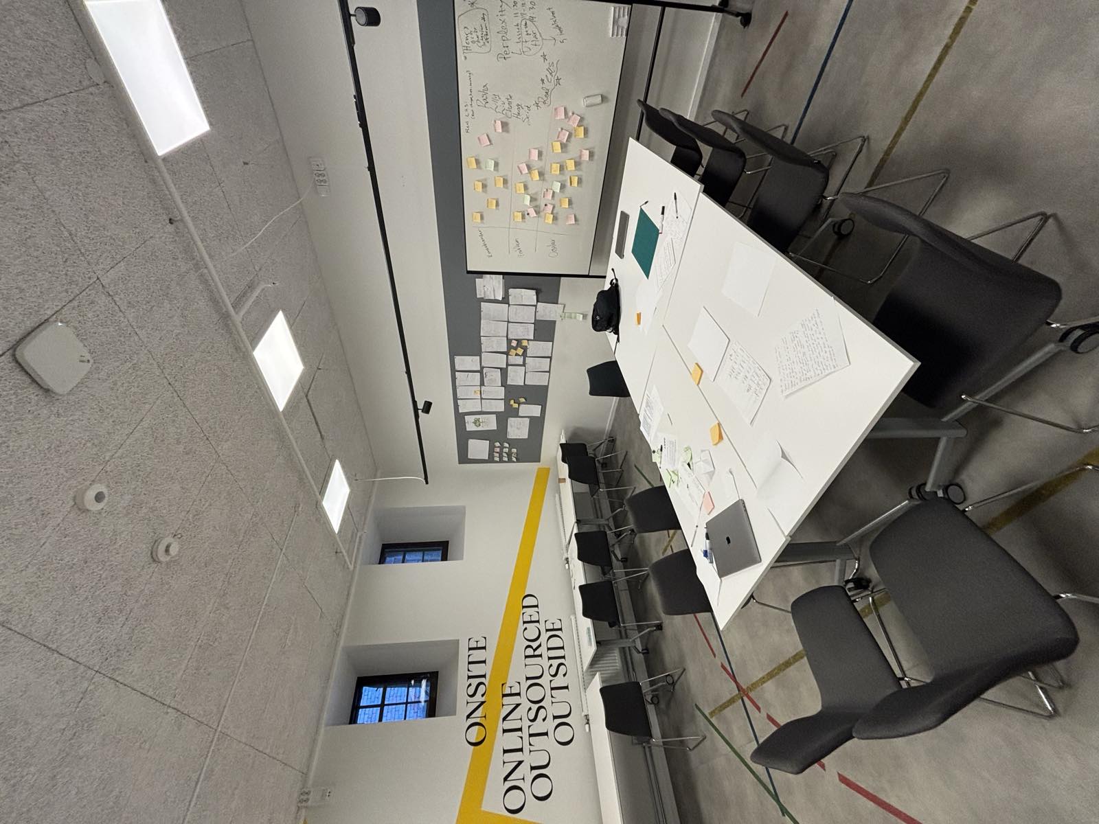 A team room at Berghs: tables with notes and a laptop, a whiteboard of sticky notes and a wall of printouts