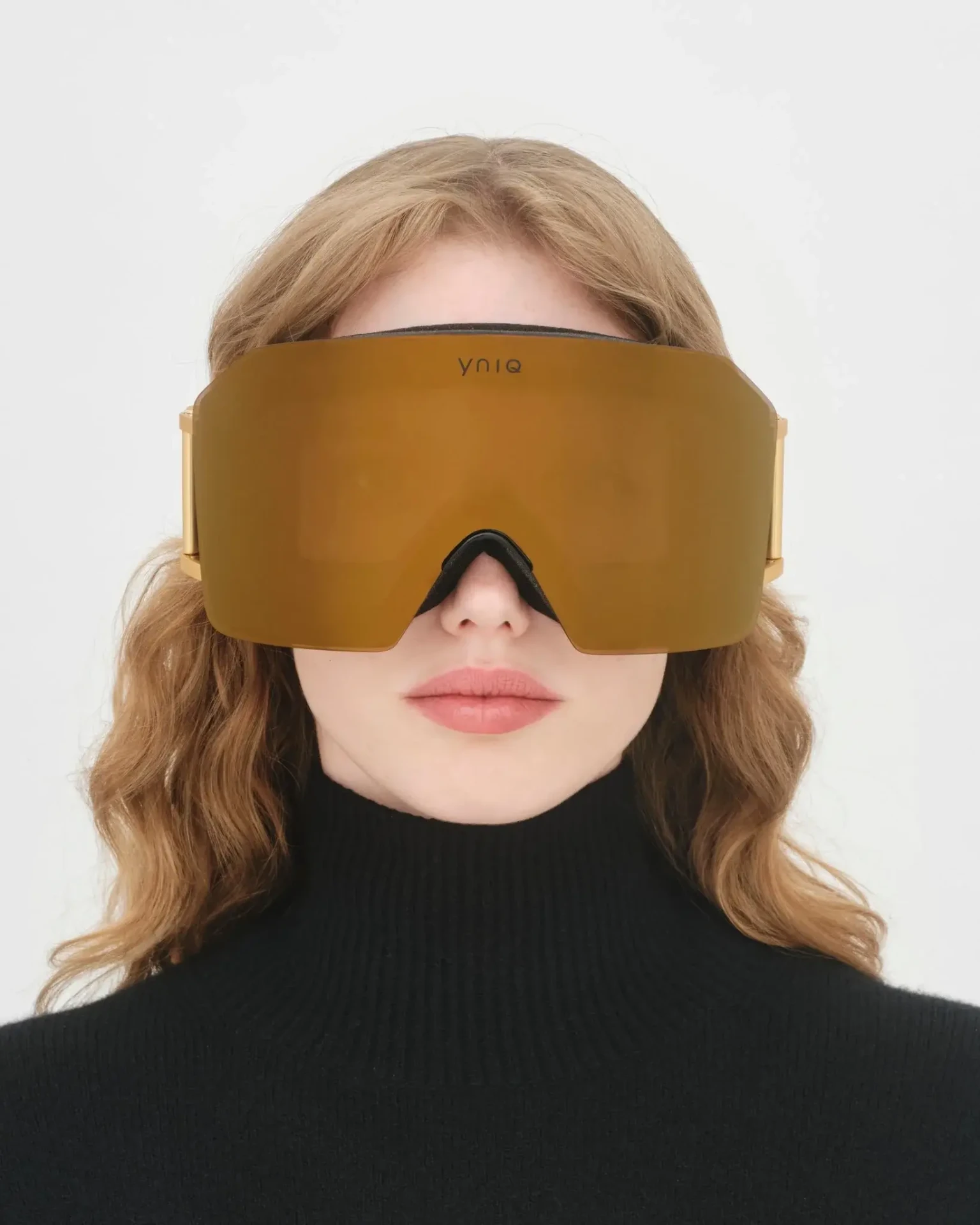 Model wearing YNIQ ski goggles with a gold mirrored lens